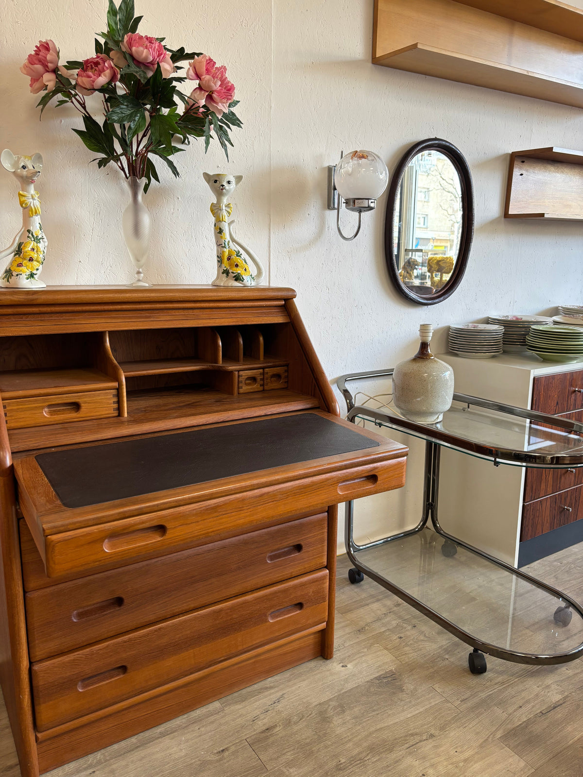 Intérieur vintage avec secrétaire en teck, soliflores en céramique en forme de souris, desserte en métal et verre des années 70, et vaisselle rétro.